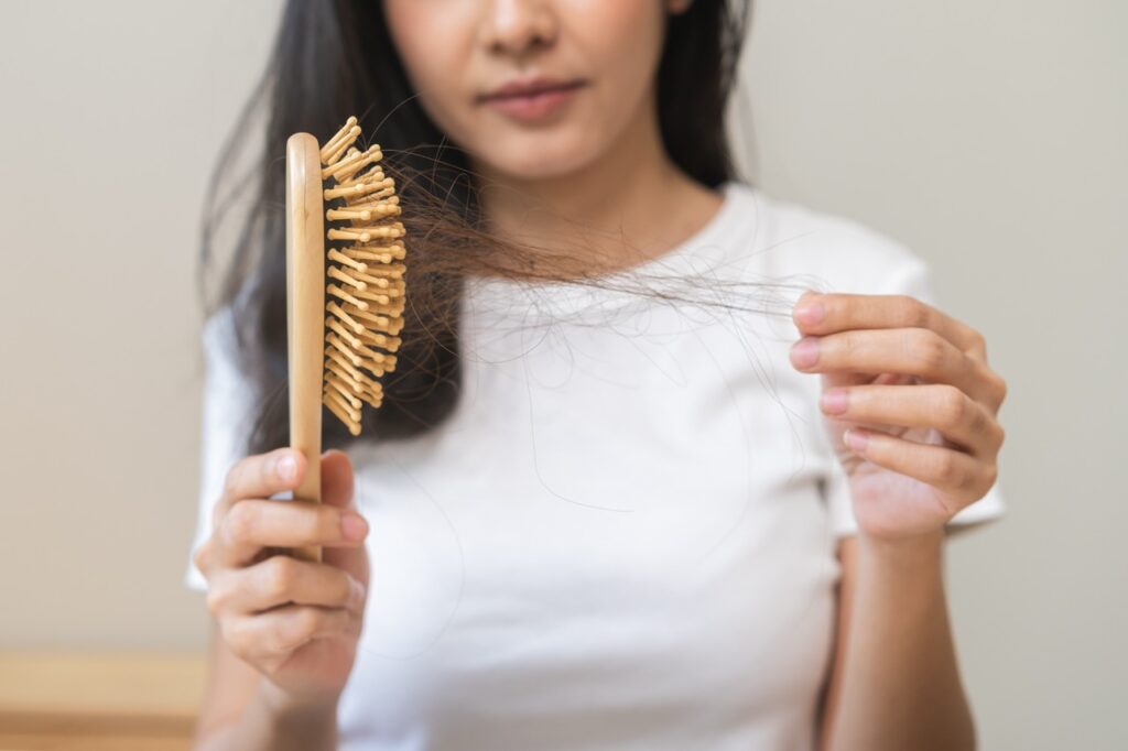 Serious woman holding brush holding comb, hairbrush with fall black hair from scalp after brushing, looking on hand worry about balding.